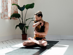 A woman holding a cat close to her while sitting on a yoga mat.