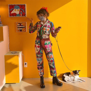 Woman and her small black and white dog stand against a yellow wall.