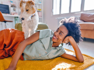 Young woman and her dog enjoying together rays of sunshine in a living room.