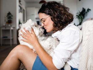 Woman kissing her small white dog at home.