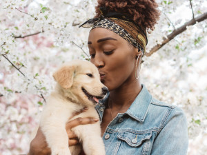 woman draped in an orange blanket holds a black-and-white puppy